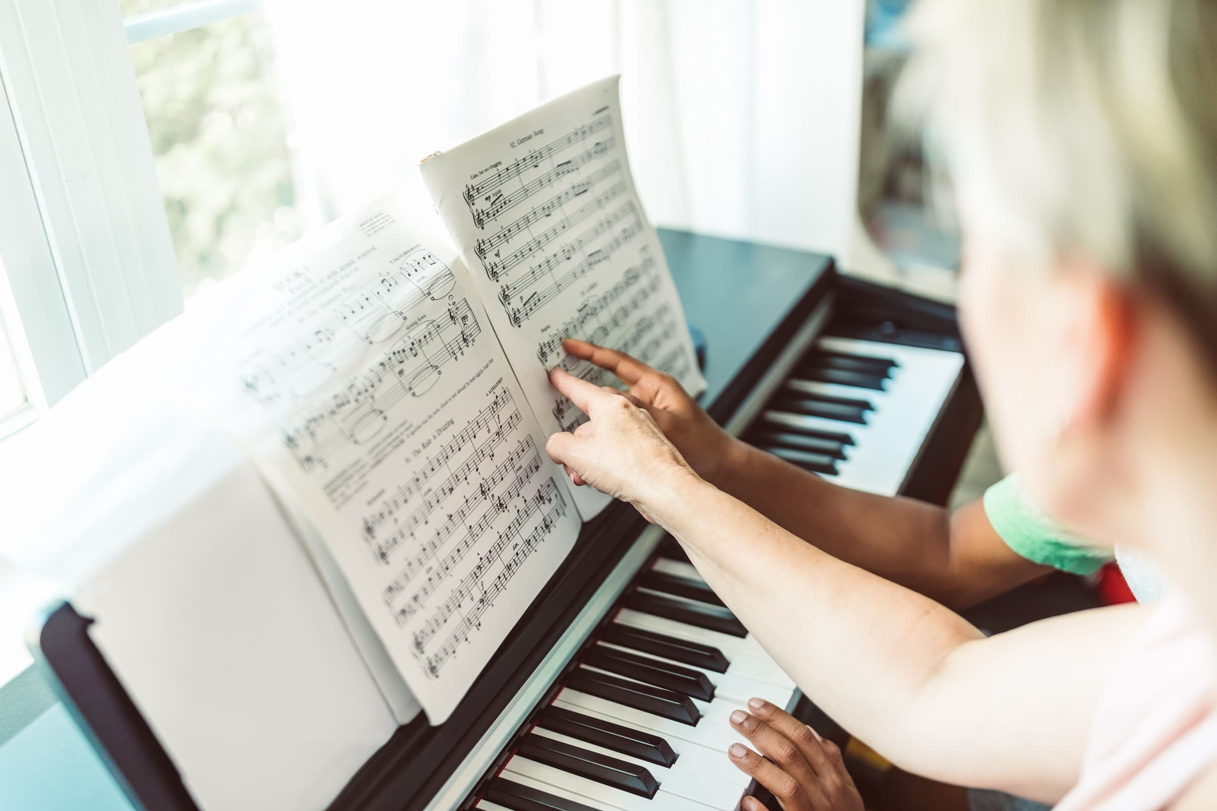 A piano lesson in progress — a teacher pointing at the score while a student plays