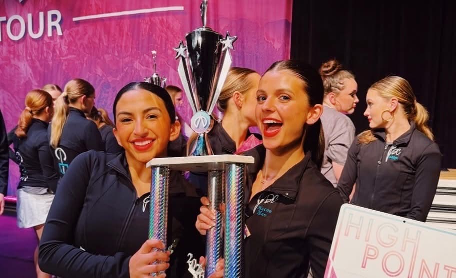 Two Continuum dancers in team jackets holding a competition trophy beside a High Point award sign