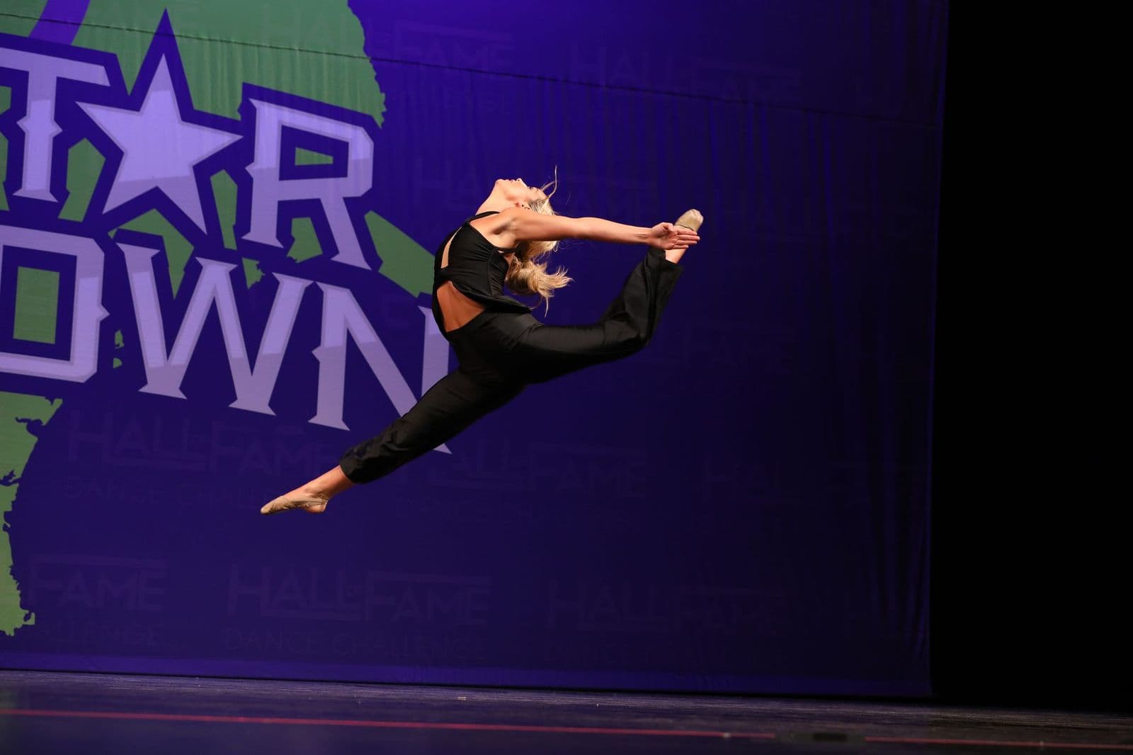 A soloist mid-leap in a black costume on a competition stage